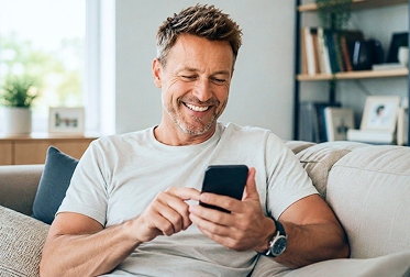 Mann sitzt lächelnd auf dem Sofa und bestellt über sein Smartphone