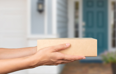 Hände halten ein Paket, im Hintergrund ist eine Haustür