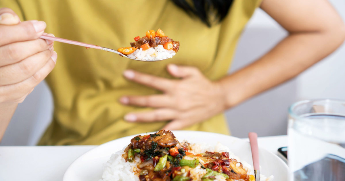 A woman eating spicy food and clutching her stomach