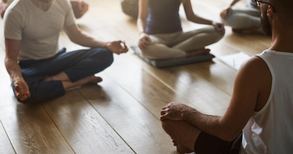 Men and women sitting cross-legged on the floor in a yoga class.