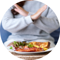 A woman crosses her arms in front of a plate of food.