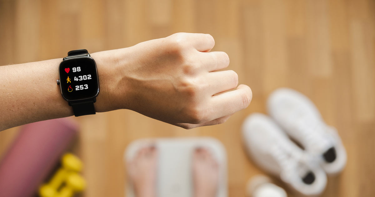 Woman on scales looking at fitness tracker watch.