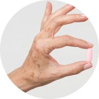 Close-up of a hand holding a pink capsule between the index finger and thumb