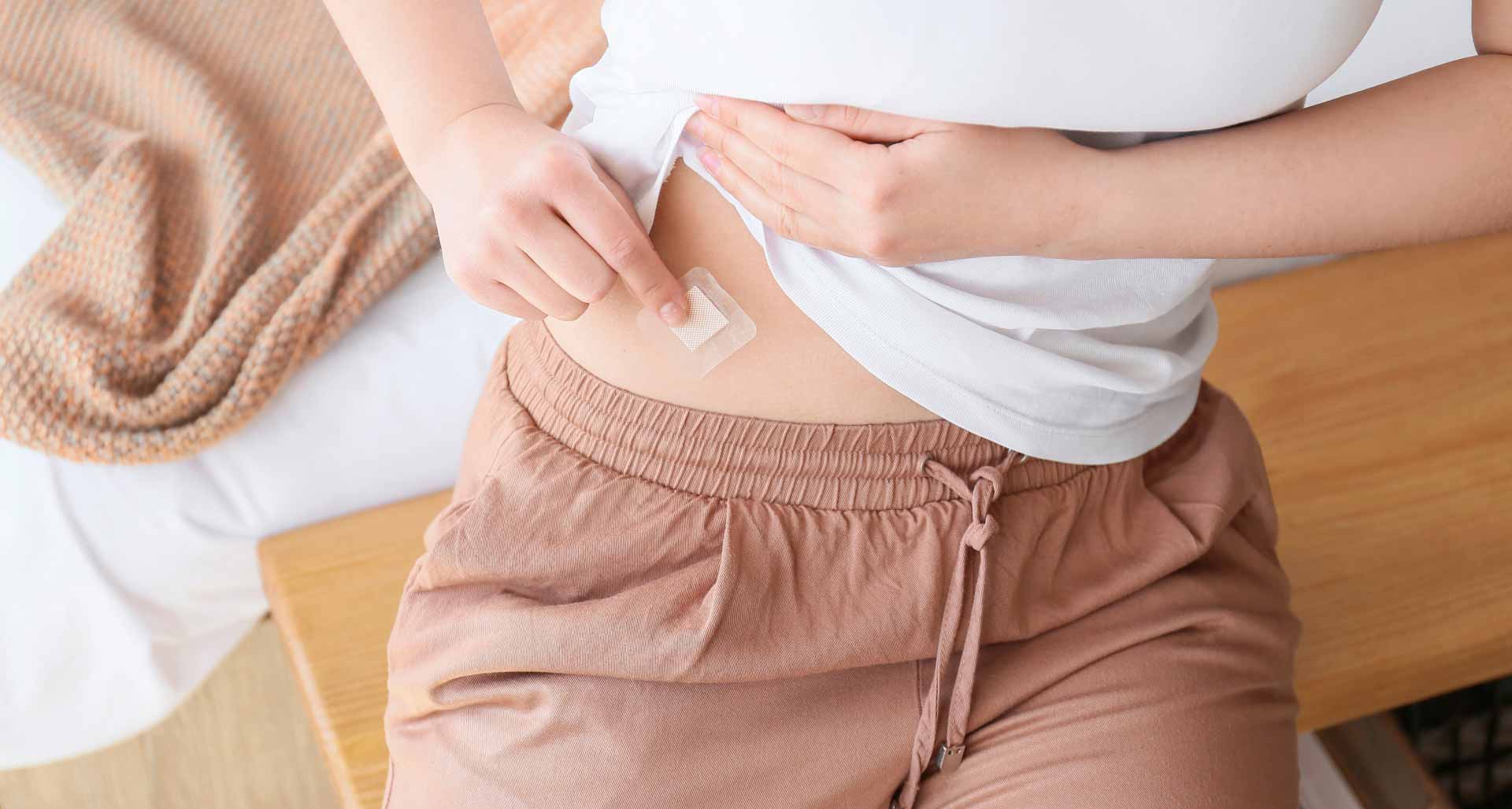 A close-up of a woman applying a patch to her stomach.