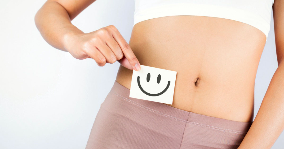 Photo of a woman’s abdomen with a smiley face picture indicating good gut health. 